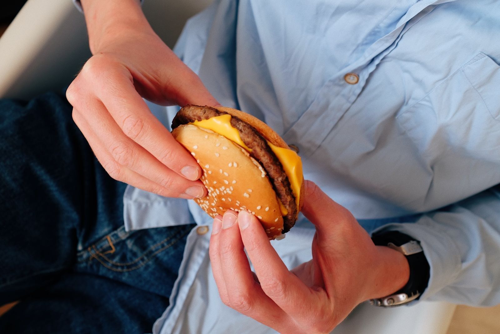 Mãos segurando um cheeseburguer mordido