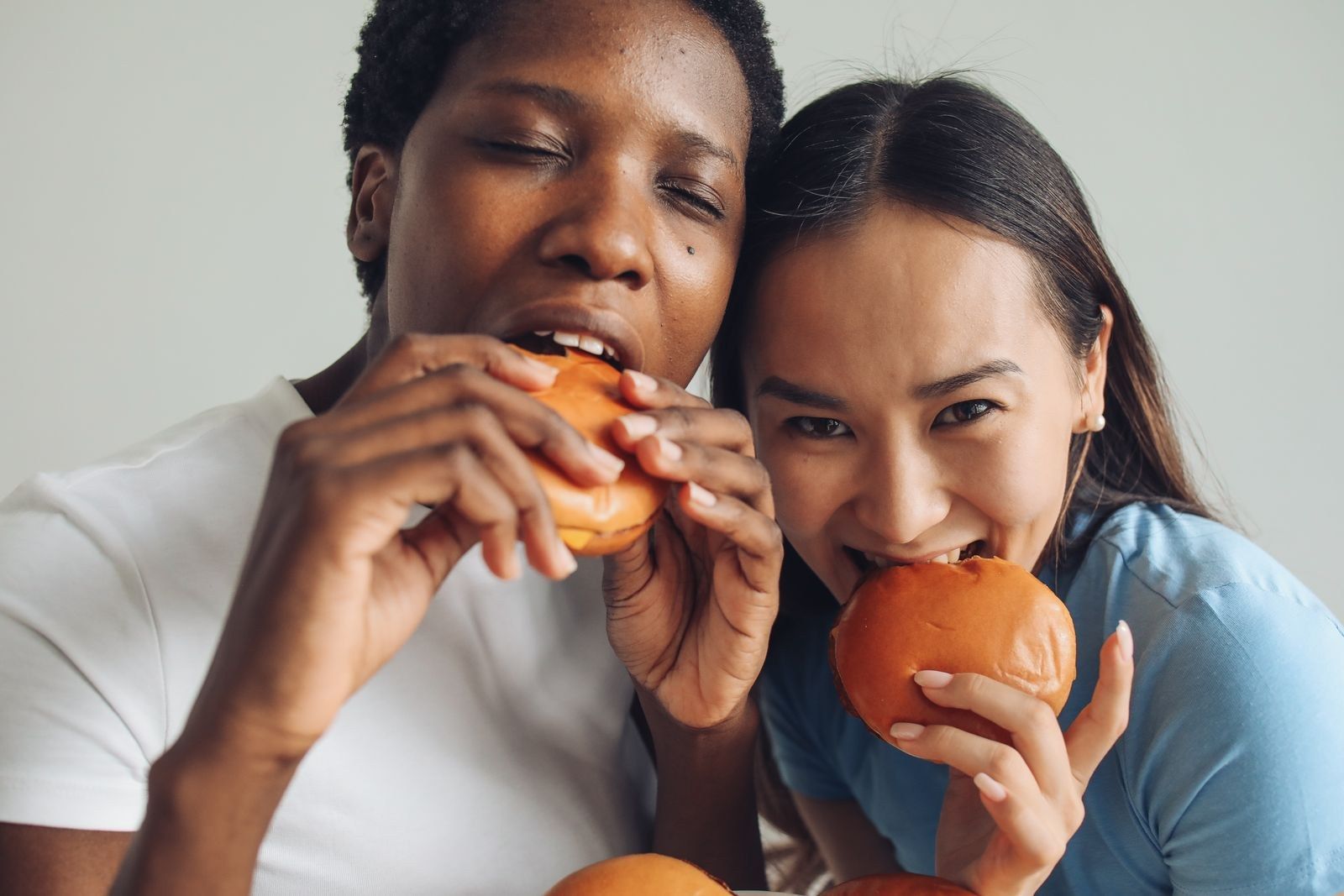 Duas amigas comendo hambúrguer juntas, sorrindo